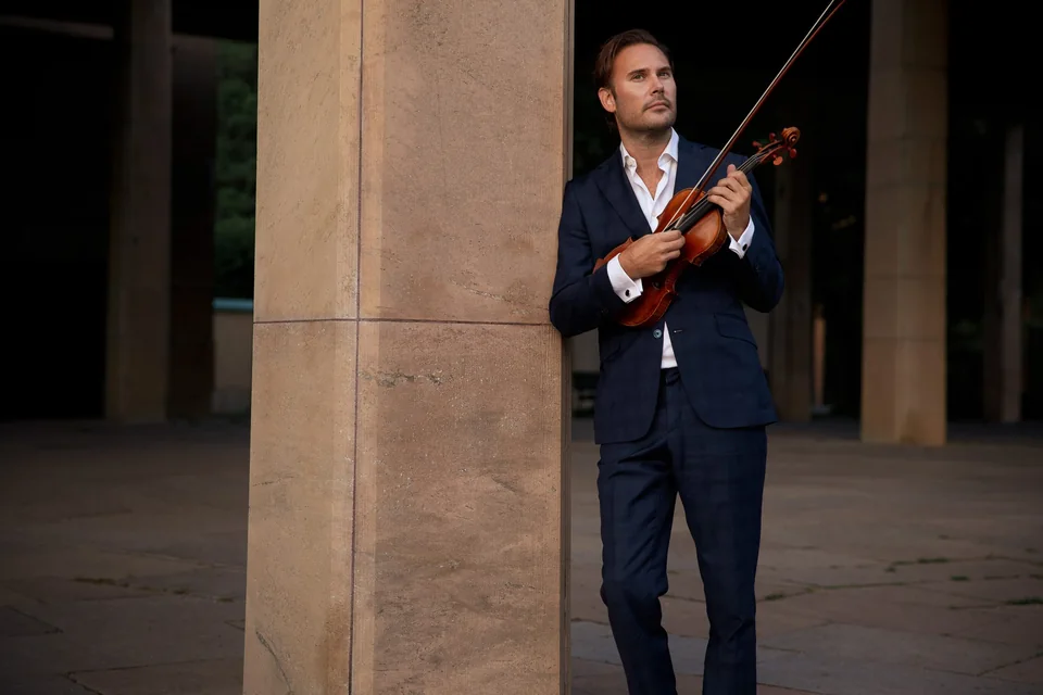 Christian Svarfvar med sin violin vid en stenpelare