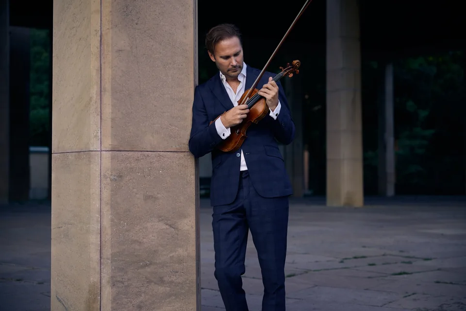 Christian Svarfvar spelar violin utomhus i blå kostym