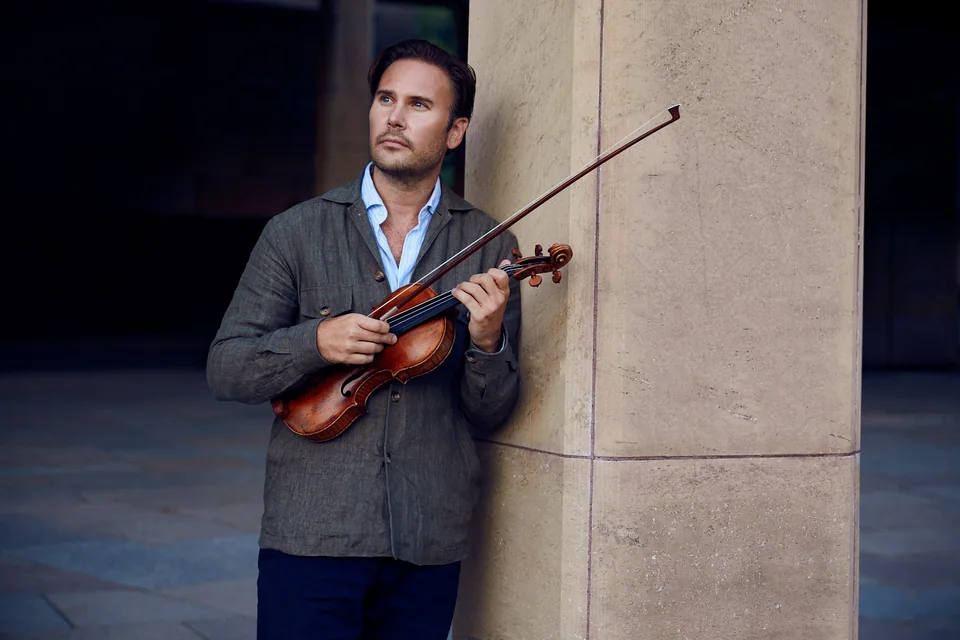 Christian Svarfvar med sin violin vid en stenpelare
