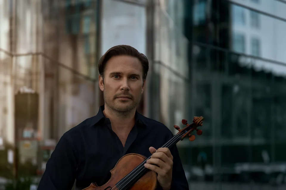 Christian Svarfvar med violin framför en stenbyggnad